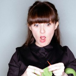 Woman with a surprise expression as she knits bright green wool.