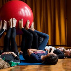 Children led on the floor in a circle holding a large ball up in the air with their feet.